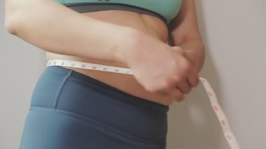 Daktilo yazan kadının kilolu konsepti ve kilo verme konsepti ölçü bandıyla belini ölçer.