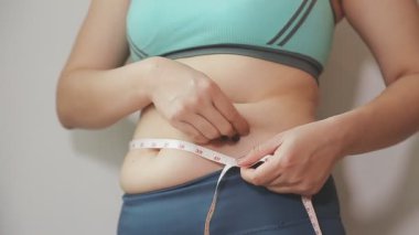 Daktilo yazan kadının kilolu konsepti ve kilo verme konsepti ölçü bandıyla belini ölçer.
