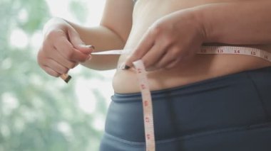 Aşırı kilolu bir kadının yakın çekim görüntüsü ölçüm bandıyla belini ölçer.,