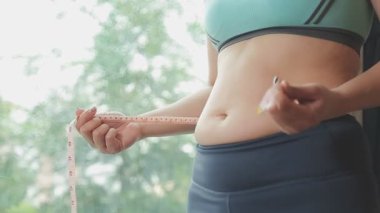 Aşırı kilolu bir kadının yakın çekim görüntüsü ölçüm bandıyla belini ölçer.,