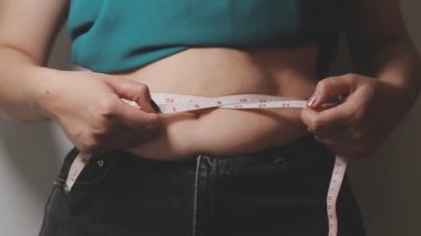Aşırı kilolu bir kadının yakın çekim görüntüsü ölçüm bandıyla belini ölçer.,
