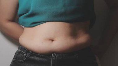 Aşırı kilolu bir kadının yakın çekim görüntüsü ölçüm bandıyla belini ölçer.,