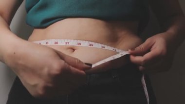 Aşırı kilolu bir kadının yakın çekim görüntüsü ölçüm bandıyla belini ölçer.,