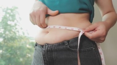 Aşırı kilolu bir kadının yakın çekim görüntüsü ölçüm bandıyla belini ölçer.,