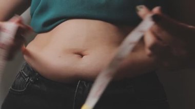 Aşırı kilolu bir kadının yakın çekim görüntüsü ölçüm bandıyla belini ölçer.,