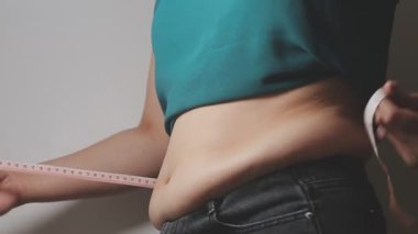 Aşırı kilolu bir kadının yakın çekim görüntüsü ölçüm bandıyla belini ölçer.,