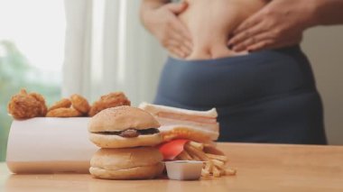 Elinde fast food tutan Asyalı bir kadın aşırı kilolu olma ve sağlıksız beslenmenin etkisini vurguluyor..