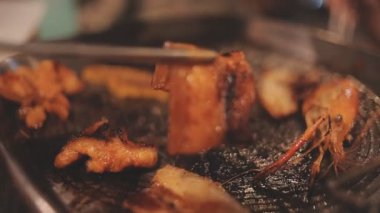 İnsanlar restoranda geleneksel Yakiniku usulü ızgara et ve karides pişiriyor..