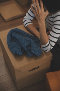 İki Asyalı blogcu, dükkanında canlı yayın yapan videoyu kaydetmek için kameranın önünde kıyafetlerini gösteriyor. Çevrimiçi alışveriş arabası fikri. Evdeki kanepede.