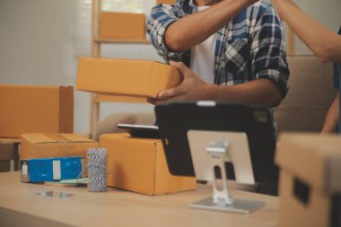 İki Asyalı blogcu, dükkanında canlı yayın yapan videoyu kaydetmek için kameranın önünde kıyafetlerini gösteriyor. Çevrimiçi alışveriş arabası fikri. Evdeki kanepede.