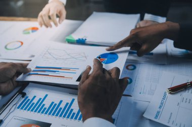 İş fikri. İş adamları konuşuyor ve başarılı takım çalışmalarının yatırım sonuçlarının büyümesini gösteren grafikler ve grafikler hakkında hesaplamalar yapıyorlar.