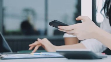 Akıllı telefonu tutan ve ofiste dizüstü bilgisayar kullanan bir kadın..