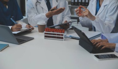 Sağlık personeli sabah toplantı odasında toplanıyor. Dijital tablete bakan doktorlar ve hemşireler.