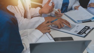 Sağlık personeli sabah toplantı odasında toplanıyor. Dijital tablete bakan doktorlar ve hemşireler.