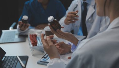 Sağlık personeli sabah toplantı odasında toplanıyor. Dijital tablete bakan doktorlar ve hemşireler.