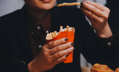 Asyalı kadın elinde patates kızartması ve restoranda mutlu bir şekilde yemek yiyor.