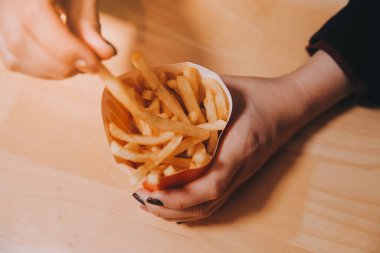 Asyalı kadın elinde patates kızartması ve restoranda mutlu bir şekilde yemek yiyor.