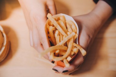 Asyalı kadın elinde patates kızartması ve restoranda mutlu bir şekilde yemek yiyor.