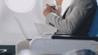 Adam havaalanında sandalyede oturuyor ve dizüstü bilgisayar kullanıyor.