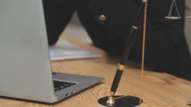 Avukat, ahşap masada dizüstü bilgisayar, tokmak ve adalet terazisiyle yeni iş sözleşmesi üzerinde çalışıyor.