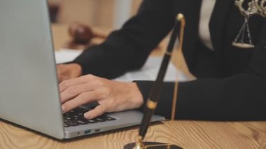 Avukat, ahşap masada dizüstü bilgisayar, tokmak ve adalet terazisiyle yeni iş sözleşmesi üzerinde çalışıyor.