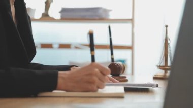 Avukat, ahşap masada dizüstü bilgisayar, tokmak ve adalet terazisiyle yeni iş sözleşmesi üzerinde çalışıyor.