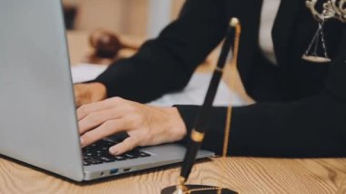 Avukat, ahşap masada dizüstü bilgisayar, tokmak ve adalet terazisiyle yeni iş sözleşmesi üzerinde çalışıyor.