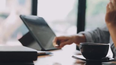 Kahve dükkanında beyaz gömlekli ve siyah ceketli genç bir kadın tablet bilgisayar ve kahve fincanıyla çalışıyor. iş kavramı.
