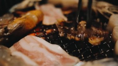 Geleneksel Yakiniku yemek stillerini kullanarak et ve karides ızgarası yapan insanların yakın çekim görüntüsü