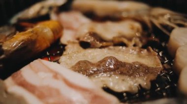 Geleneksel Yakiniku yemek stillerini kullanarak et ve karides ızgarası yapan insanların yakın çekim görüntüsü