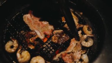 Izgarada et ve karides pişiren insanların yakın çekim görüntüsü. Yakiniku, Japonya 'da yemek yemenin çok popüler bir yoludur.. 