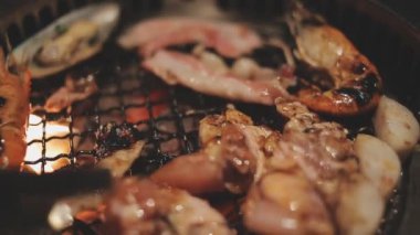 Mutfak meraklılarının et ve kabukluların bir karışımını hazırladığı yakın görüş. Yakiniku, Japonya 'nın sevilen masa başı ızgara geleneği interaktif gastronomiyi özetliyor.