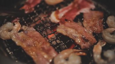 Mutfak meraklılarının et ve kabukluların bir karışımını hazırladığı yakın görüş. Yakiniku, Japonya 'nın sevilen masa başı ızgara geleneği interaktif gastronomiyi özetliyor.