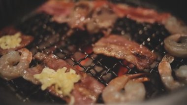 Mutfak meraklılarının et ve kabukluların bir karışımını hazırladığı yakın görüş. Yakiniku, Japonya 'nın sevilen masa başı ızgara geleneği interaktif gastronomiyi özetliyor.