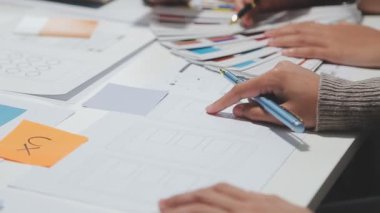 Çalışma alanı boyunca yayılmış prototip çizimleri kullanarak yeni uygulama arayüzü oluşturmada işbirliği yapan tasarım ekibi