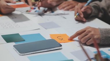 Çalışma alanı boyunca yayılmış prototip çizimleri kullanarak yeni uygulama arayüzü oluşturmada işbirliği yapan tasarım ekibi