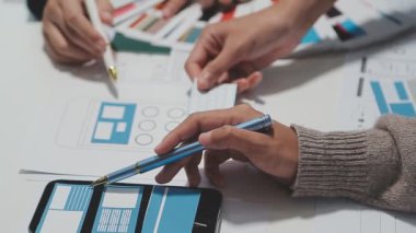 Çalışma alanı boyunca yayılmış prototip çizimleri kullanarak yeni uygulama arayüzü oluşturmada işbirliği yapan tasarım ekibi