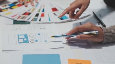 Çalışma alanı boyunca yayılmış prototip çizimleri kullanarak yeni uygulama arayüzü oluşturmada işbirliği yapan tasarım ekibi