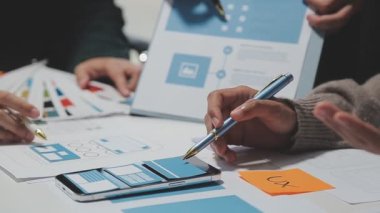Çalışma alanı boyunca yayılmış prototip çizimleri kullanarak yeni uygulama arayüzü oluşturmada işbirliği yapan tasarım ekibi