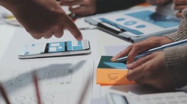Çalışma alanı boyunca yayılmış prototip çizimleri kullanarak yeni uygulama arayüzü oluşturmada işbirliği yapan tasarım ekibi