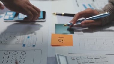 Çalışma alanı boyunca yayılmış prototip çizimleri kullanarak yeni uygulama arayüzü oluşturmada işbirliği yapan tasarım ekibi