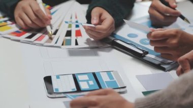 Çalışma alanı boyunca yayılmış prototip çizimleri kullanarak yeni uygulama arayüzü oluşturmada işbirliği yapan tasarım ekibi