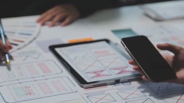 Çalışma alanı boyunca yayılmış prototip çizimleri kullanarak yeni uygulama arayüzü oluşturmada işbirliği yapan bir grup genç şarkıcı
