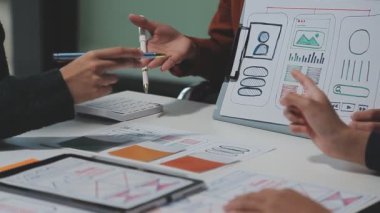 Çalışma alanı boyunca yayılmış prototip çizimleri kullanarak yeni uygulama arayüzü oluşturmada işbirliği yapan bir grup genç şarkıcı