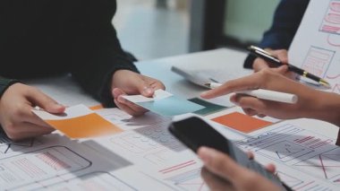 Çalışma alanı boyunca yayılmış prototip çizimleri kullanarak yeni uygulama arayüzü oluşturmada işbirliği yapan bir grup genç şarkıcı