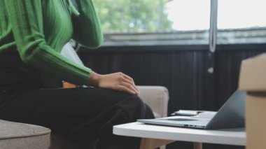 Kadın dizüstü bilgisayar tutuyor ve evdeki oturma odasında kanepeye posta yolluyor. Teslimat konsepti. Akıllı telefon kullanan kadın