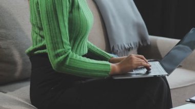 Dizüstü bilgisayarı olan kadın kanepenin yanında oturuyor.