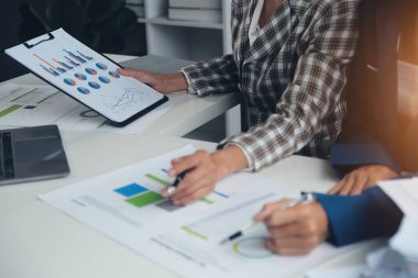 Group of confident business people point to graphs and charts to analyze market data, balance sheet, account, net profit to plan new sales strategies to increase production capacity.