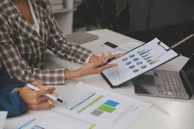 Group of confident business people point to graphs and charts to analyze market data, balance sheet, account, net profit to plan new sales strategies to increase production capacity.