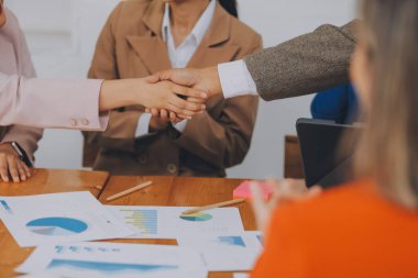 Bir grup iş adamı mutlu ve kendinden emin gülümsüyor. Birlikte çalışırken gülümseyerek ofiste el sıkışırken.